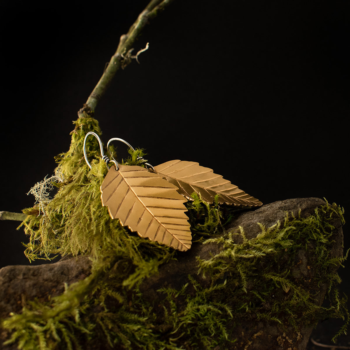 The Brass Alder Leaf Earrings both lying down, showing their intricately serrated edges sawn out from sheet metal, and veins stamped and patinated by hand.