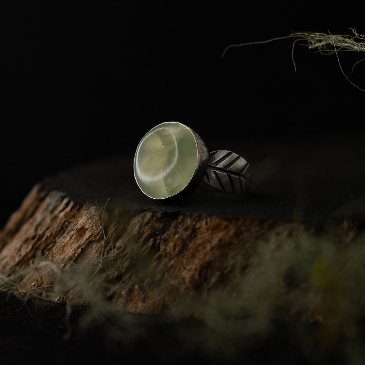 A handmade sterling silver statement ring, with a setting of vibrant light green prehnite, and elements textured to look like small leaves.