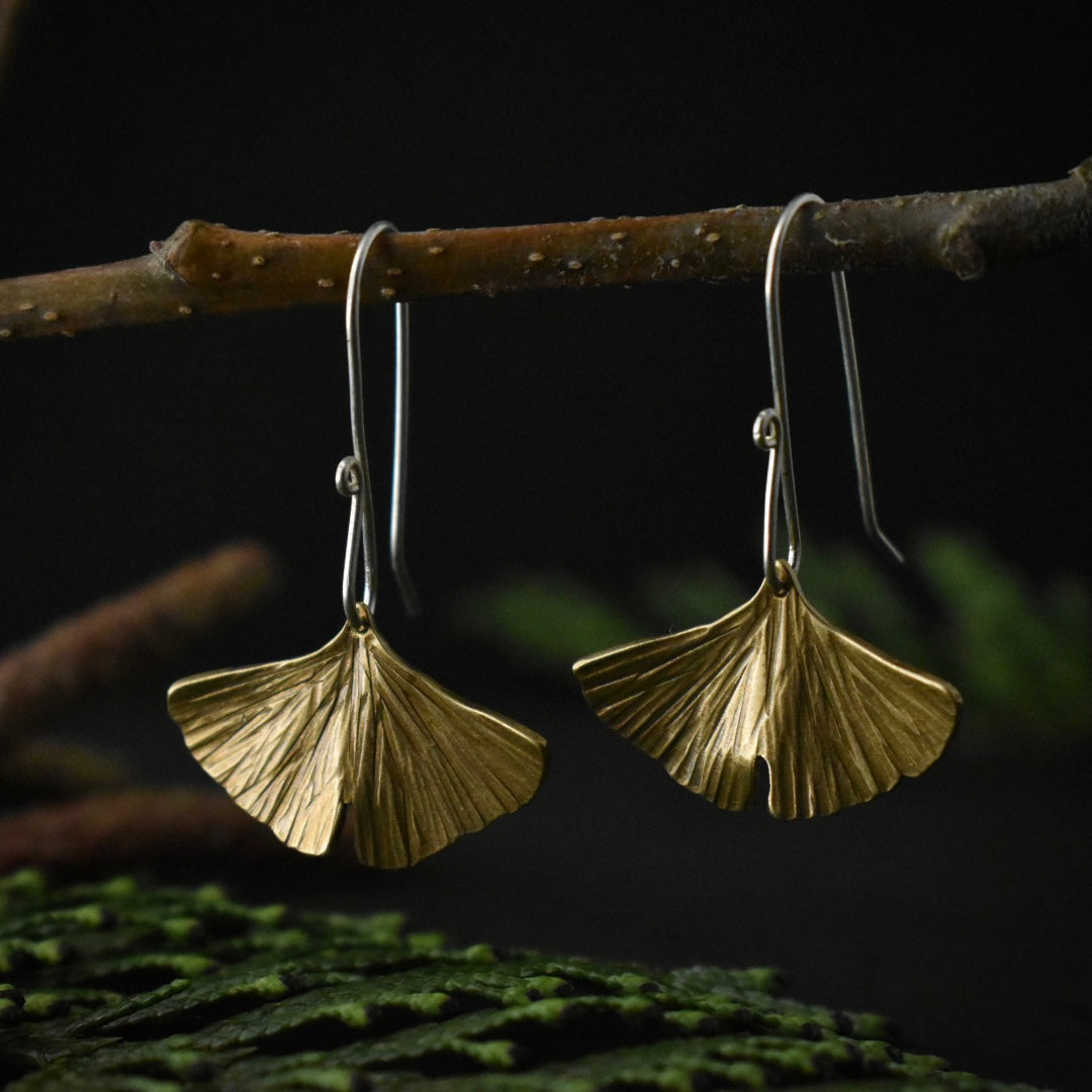 A pair of handmade shiny brass dangle earrings, each stamped and textured to look like a gingko leaf.