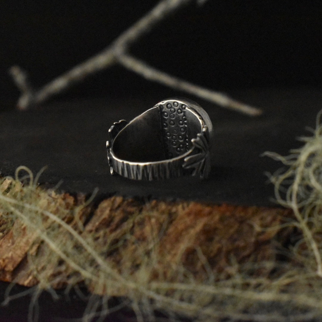 The back of the Real Lichen Double Oak Leaf Ring, showing the details stamped underneath the setting and its tapered size 7 3/4 sterling silver ring band, textured to look like tree bark.