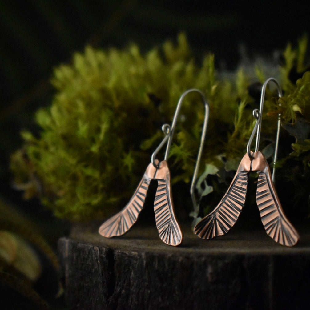 A three-quarter view of the Copper Helicopter Earrings, showing their sterling silver ear wires.