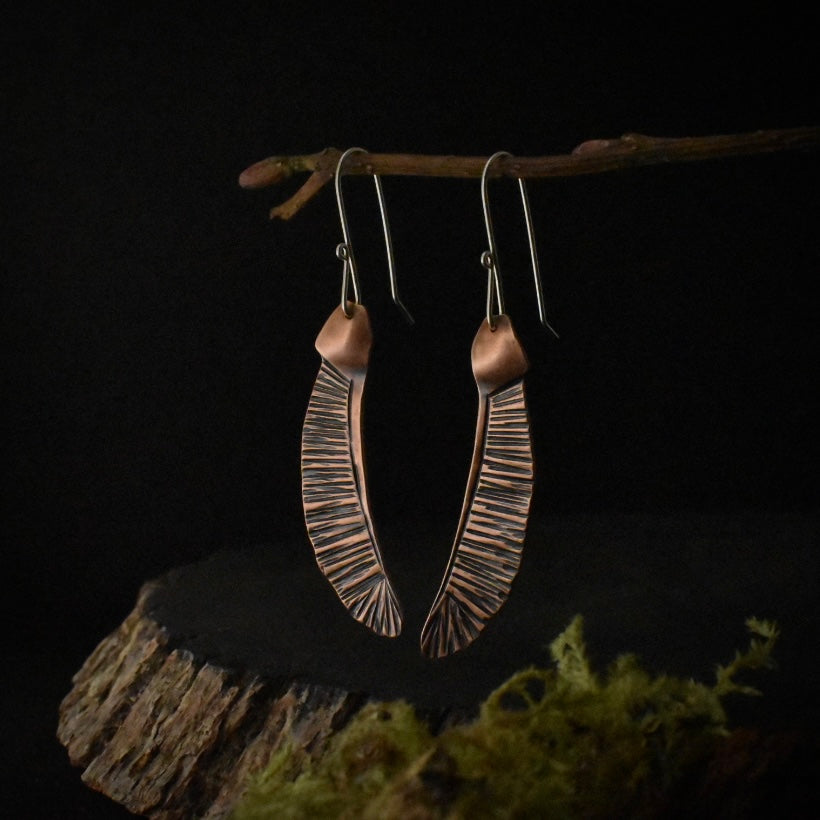 A pair of copper dangle earrings, each stamped and textured to look like a maple seed.