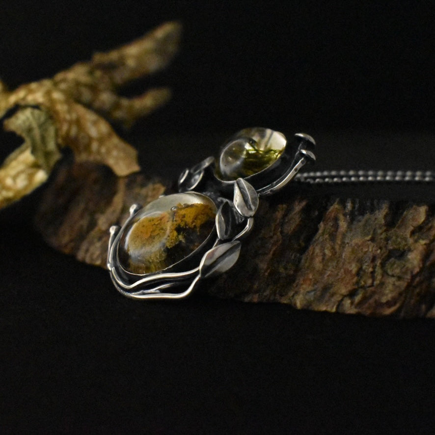 A three-quarter view of the Lichen Love Pendant, showing its sterling silver elements, textured and formed to look like mushrooms, grass, and lichen.