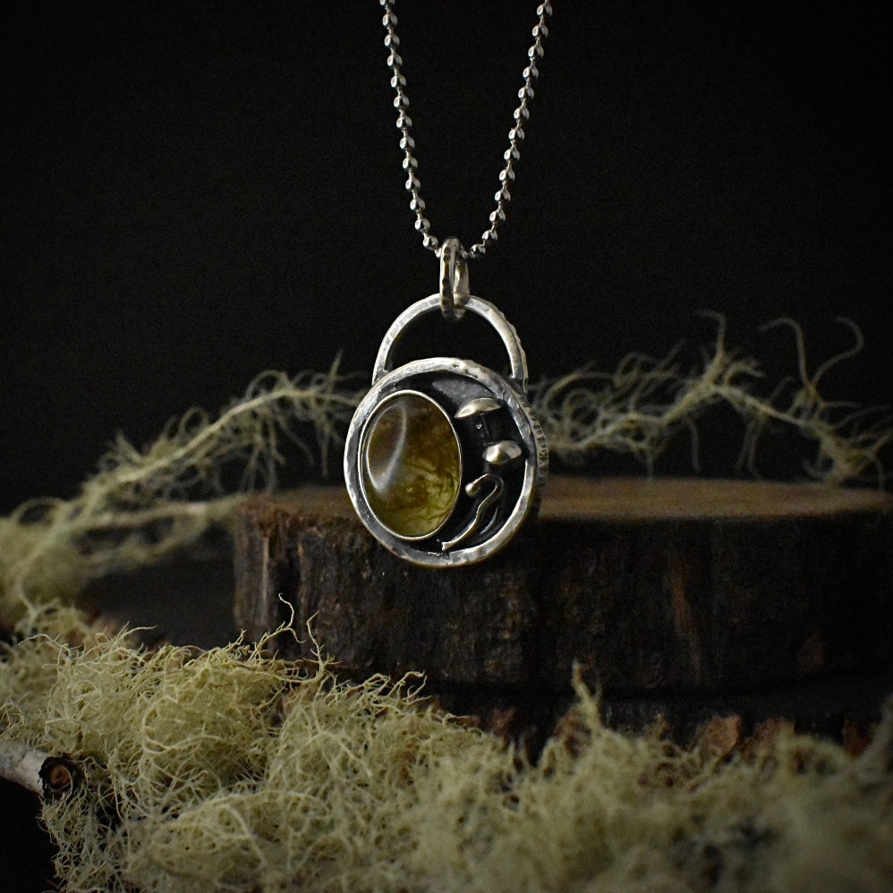 A handmade sterling silver pendant necklace, with a large setting of real moss preserved in clear resin, hanging by a stainless steel ball chain.