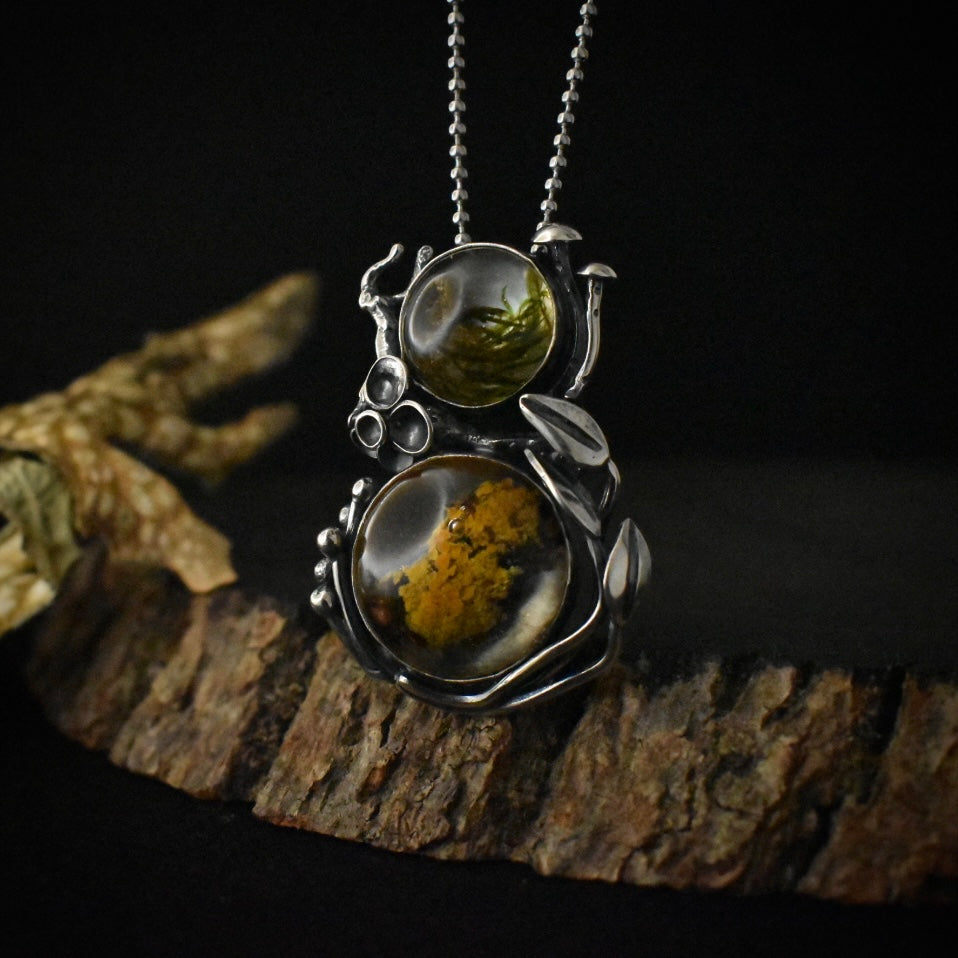 A handmade sterling silver pendant necklace, with two large settings of real moss and lichen preserved in clear resin, hanging by a stainless steel ball chain.