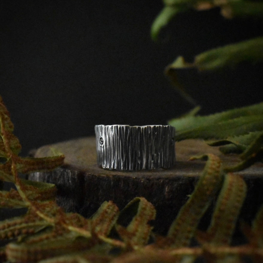 A handmade sterling silver wide band ring, stamped and textured to look like tree bark.