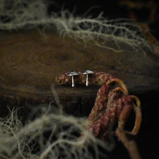 A pair of handmade sterling silver stud earrings, each formed and textured to look like a small mushroom.