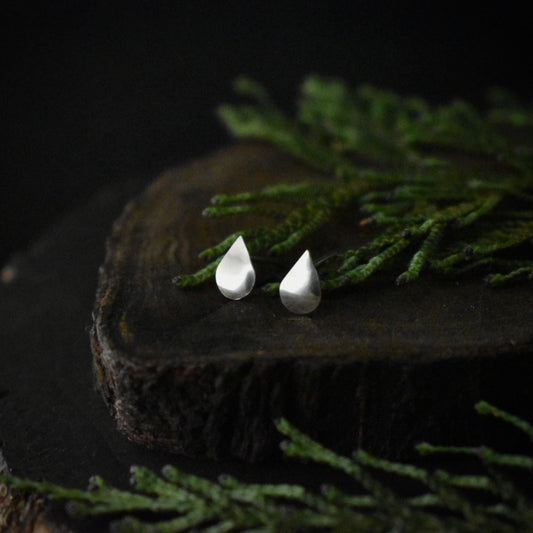 A pair of handmade sterling silver stud earrings, each formed to look like a raindrop.