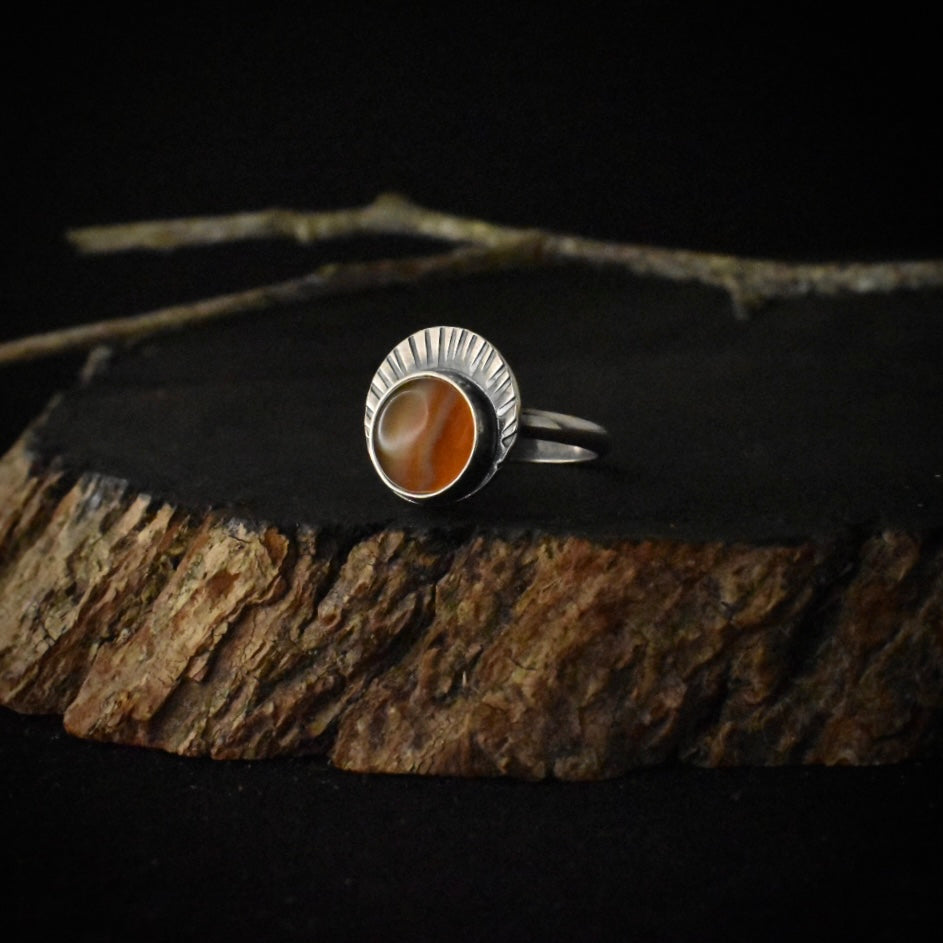 A handmade sterling silver statement ring, with a setting of bright orange banded agate, and stamped radiating lines.