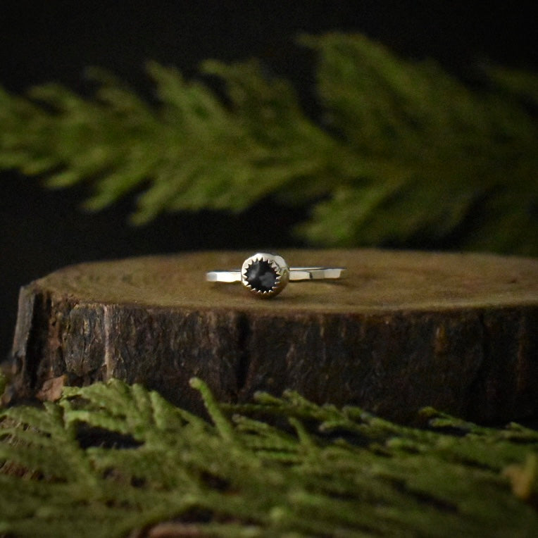 A handmade sterling silver stackable solitaire ring, with dark snowflake obsidian in a small serrated bezel setting.