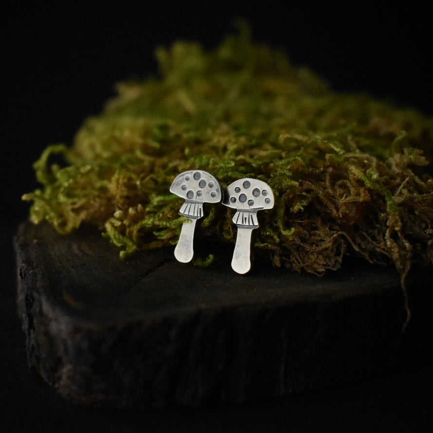 A pair of handmade sterling silver stud earrings, each stamped flat and textured to look like an amanita mushroom.