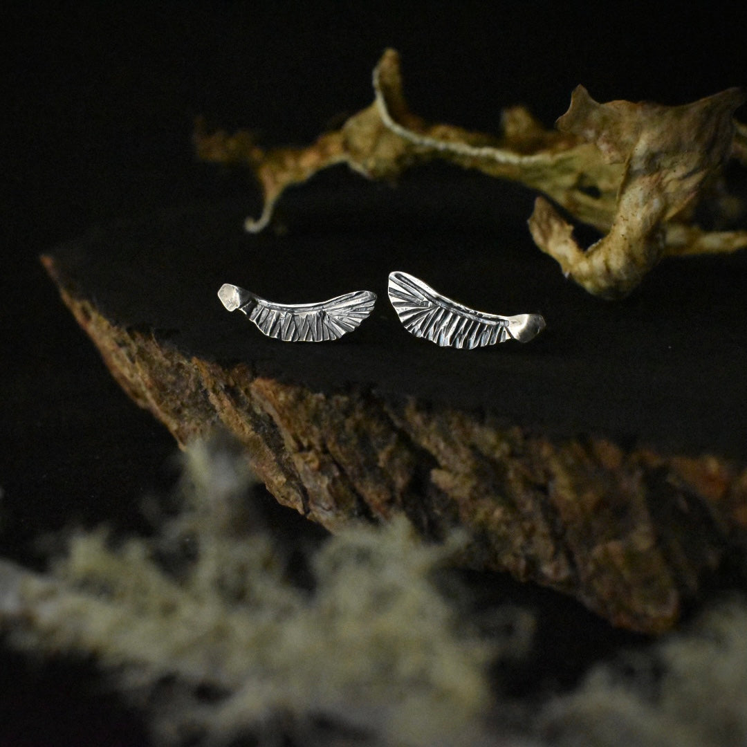 A pair of handmade sterling silver stud earrings, each stamped and textured to look like a maple seed.