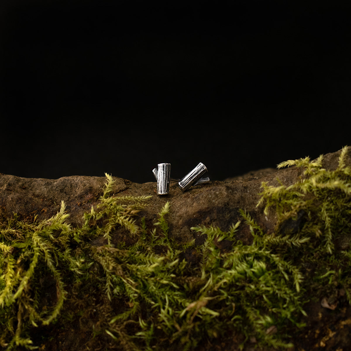 Two teeny tiny sterling silver stud earrings sit side by side, each a miniature sculpture formed like a wooden log.