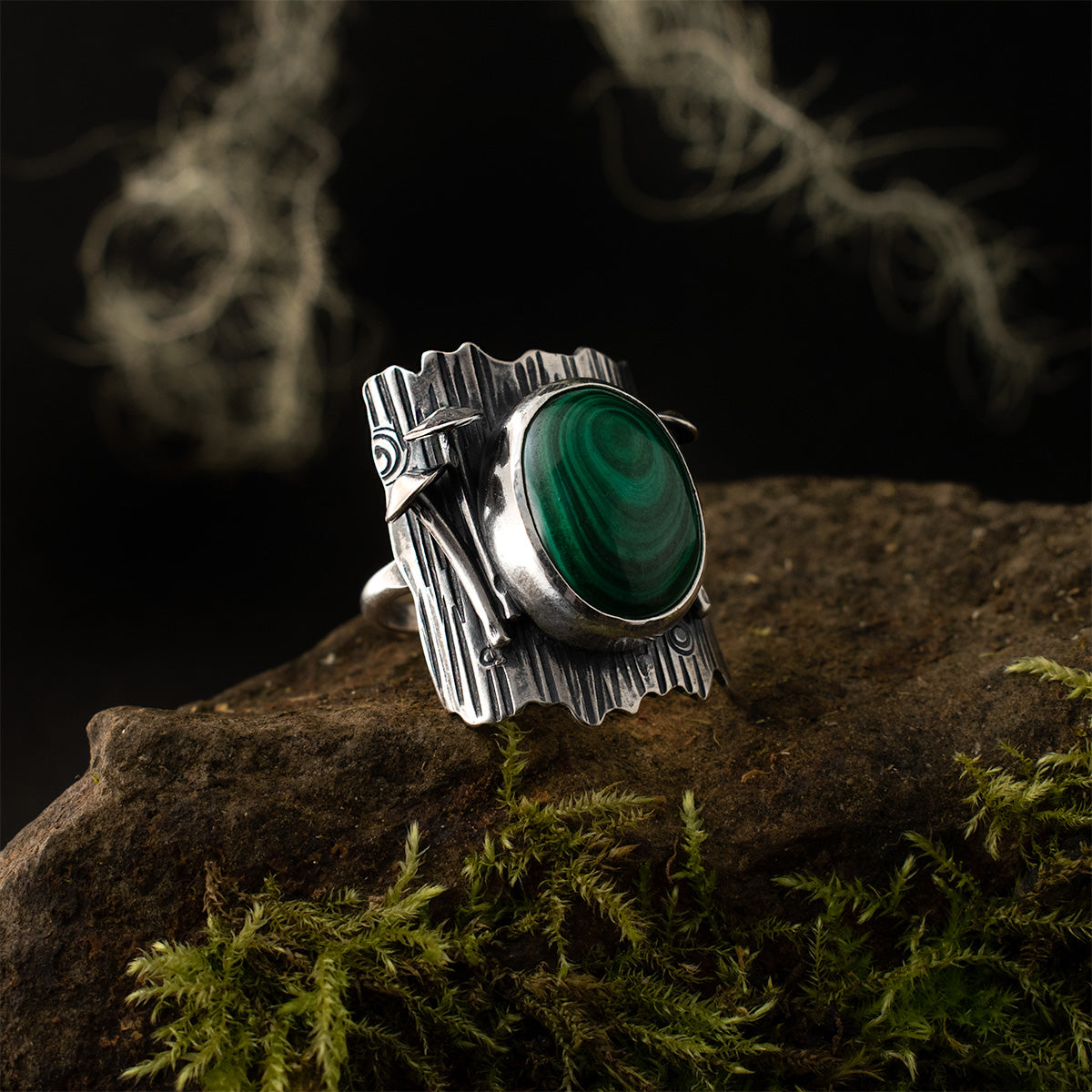 The left side of the Malachite Tree Trunk Ring, two of its 3D fungi, and its swirling stone are all set on a sterling silver shield textured like tree bark.