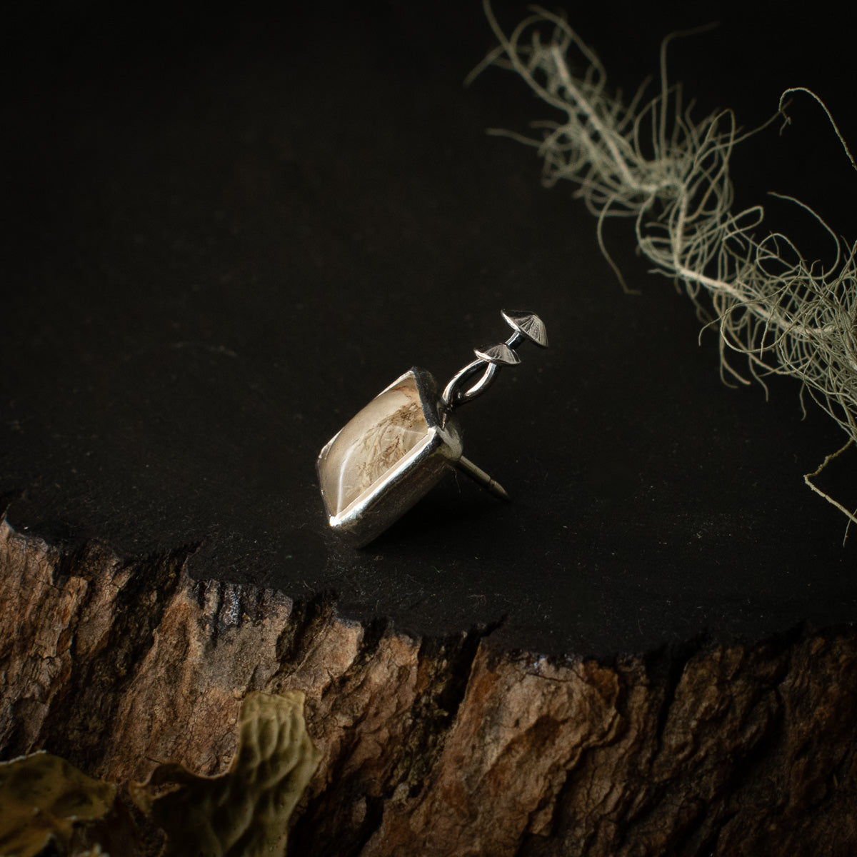 The right side of the Real Lichen Mycena Duo Lapel Pin, showing its sterling silver elements, formed to look like two intertwining mushrooms.