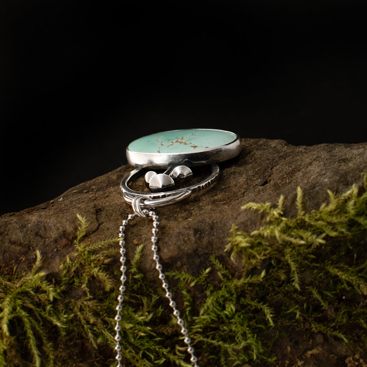 The top side of the Turquoise Fungal Loop Pendant while it lies down, showing its smooth mushroom caps and sterling silver loop, textured by hand like tree bark.